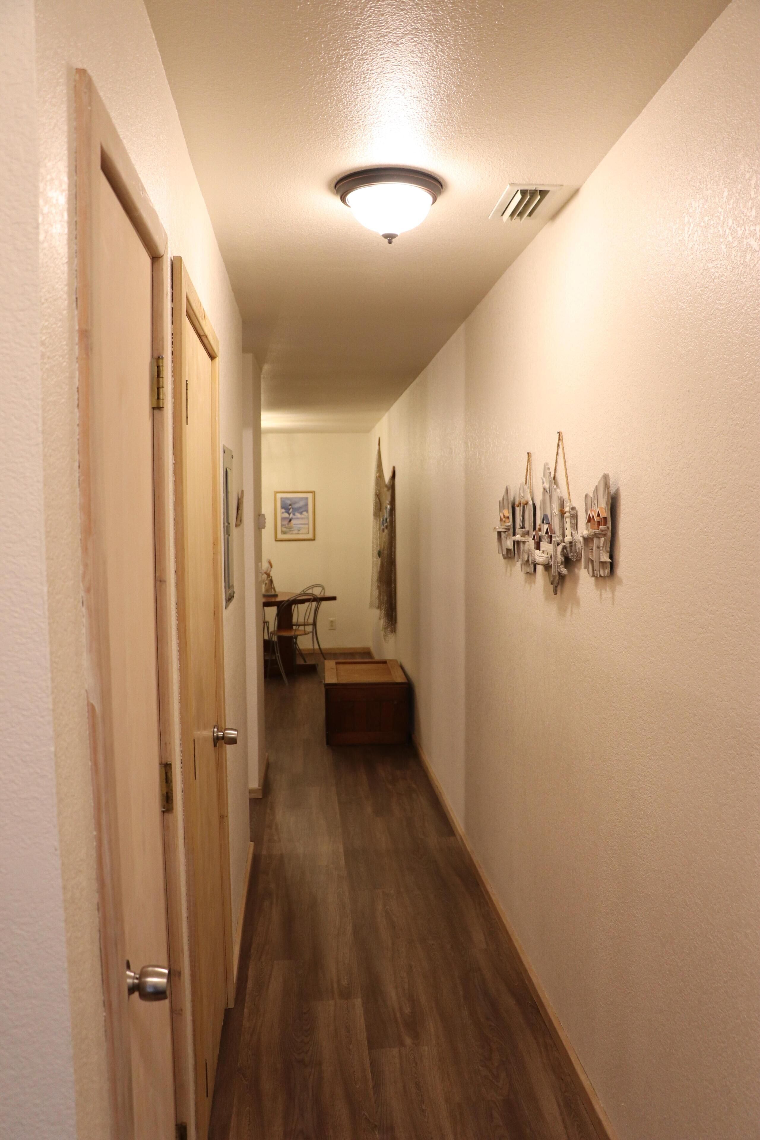 A hallway with wooden flooring, a ceiling light, and a wall-mounted artwork.