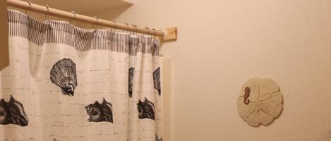 A bathroom with a toilet, a shower curtain with sea-themed designs, and a toilet paper holder.
