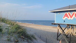 Eine Strandlage mit einer Holzterrasse und einem Gebäude mit dem Schriftzug 'AVON'.