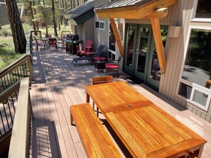 Terraza de madera con mesa, bancos, una parrilla y asientos al aire libre.