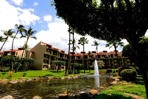 Un hotel con piscina, palmeras y una fuente.
