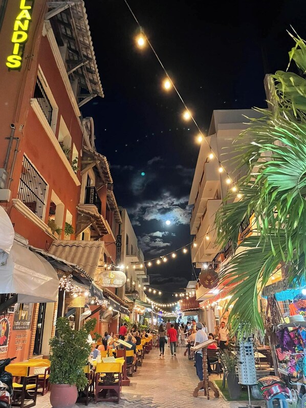Una calle bordeada de edificios, con mesas al aire libre y guirnaldas de luces.