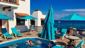A pool area with lounge chairs and umbrellas, a small pool, and a view of the ocean.
