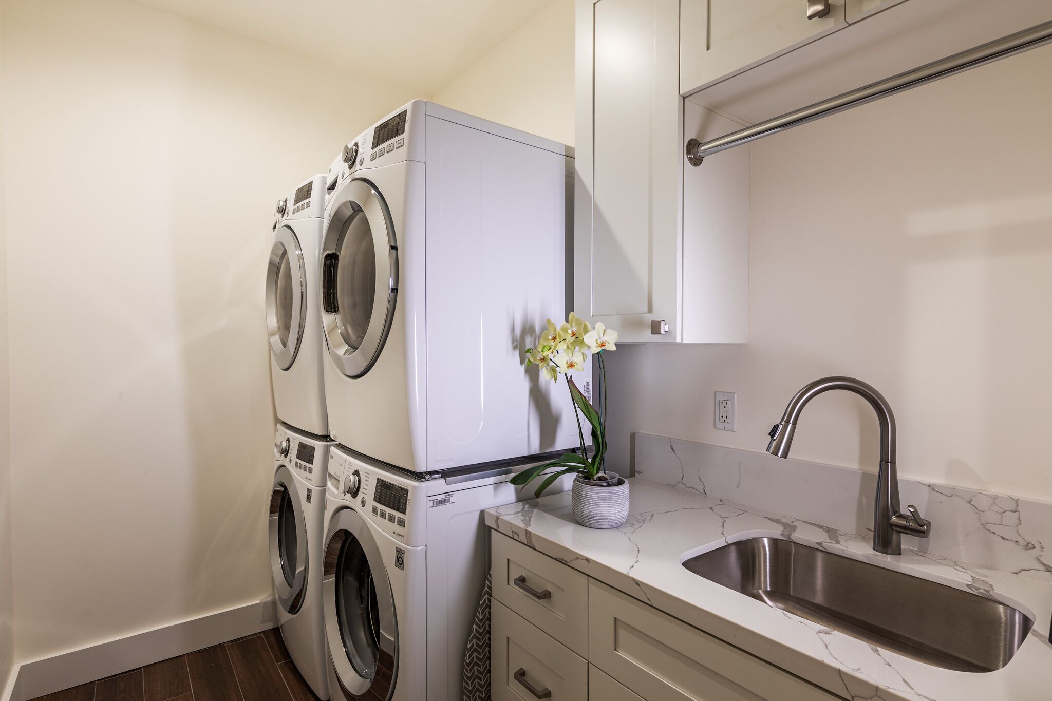 A compact laundry area with stacked washers and dryers, a marble countertop, and a modern sink.