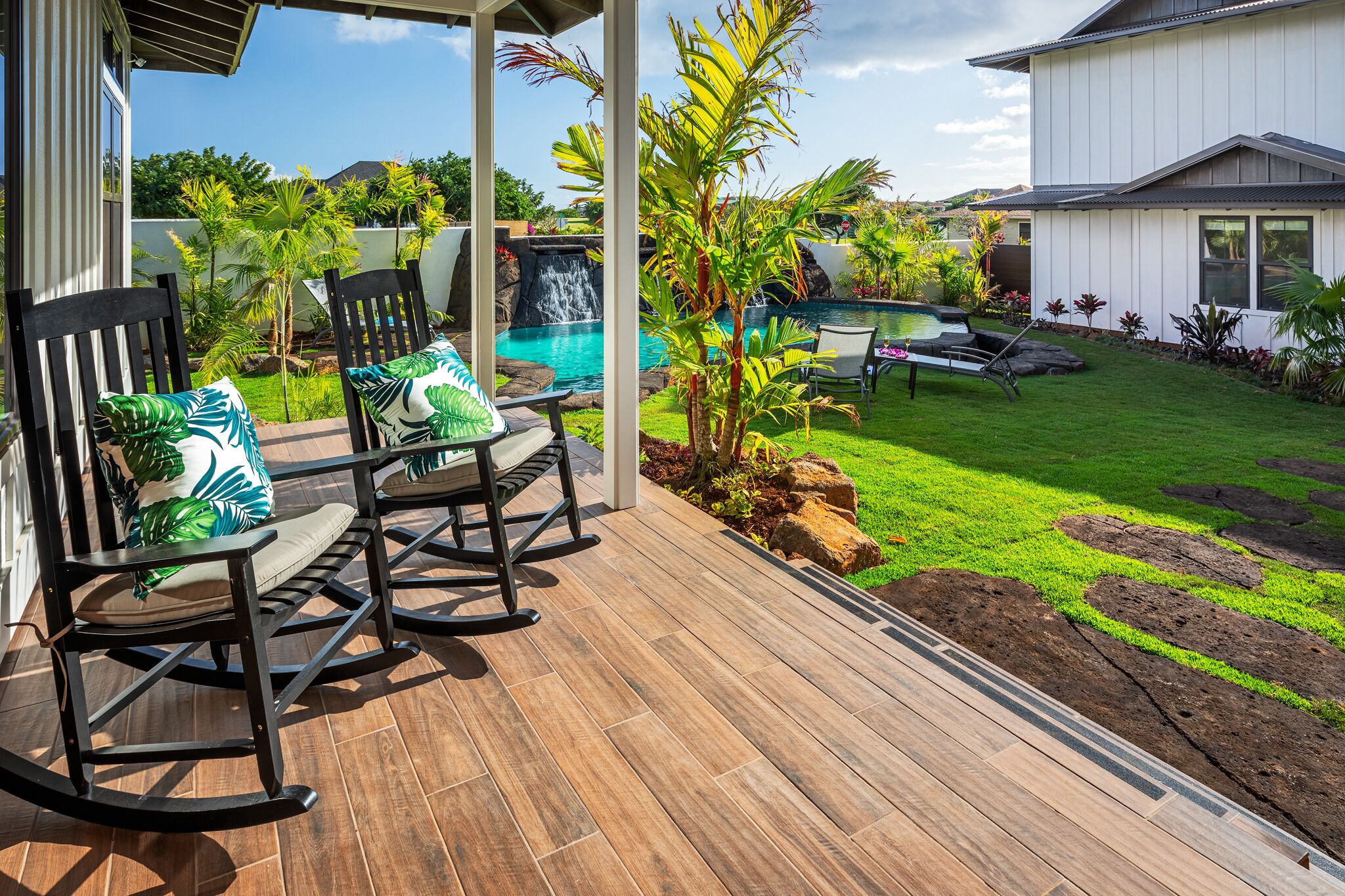 A patio with wooden flooring, rocking chairs, and a small pool area with a waterfall.