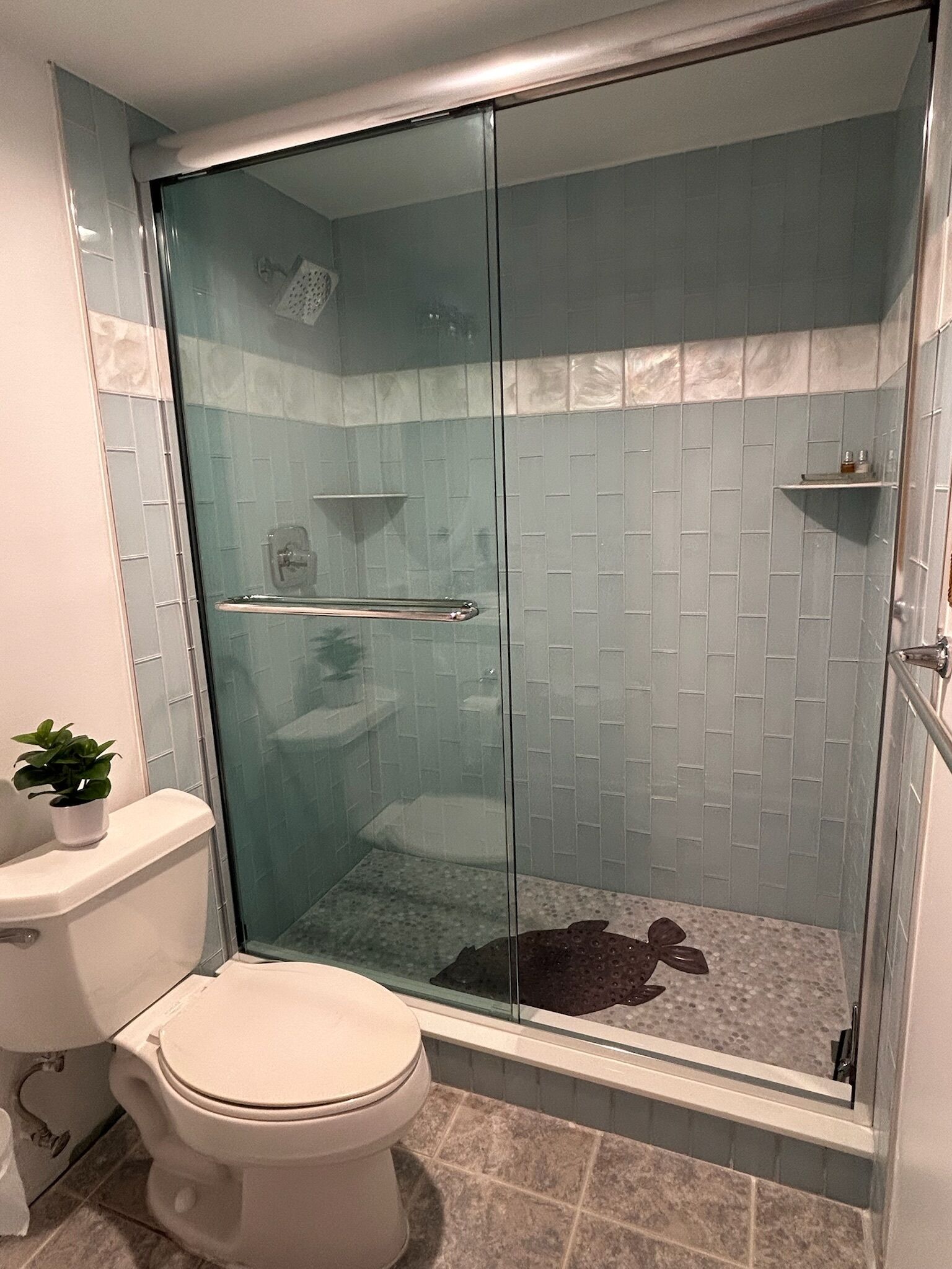 Eine begehbare, glasumrandete Dusche mit Fliesenboden, eine Toilette und eine kleine Ablage mit Toilettenartikeln.