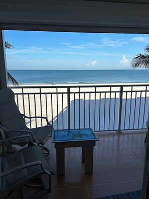 A balcony with a view of the beach, a glass table, and two lounge chairs. - Direct Gulf-Front 2 Bedroom Condo... Gulf Side Sunsets 1 (Fort Myers Beach)