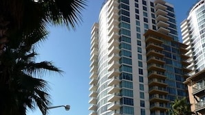 A tall, modern hotel with multiple balconies, located in an urban area with palm trees and other buildings in the background. - WEST OCEAN TOWERS Long Bch Condo 2Bed/2BA/Sunny/Balcony/ Pool/Gym/BEST BUILDING! (Long Beach)