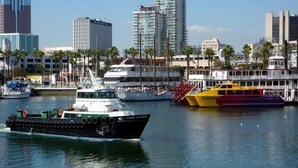 A ferry boat with a green and white hull, docked at a marina with tall buildings in the background. - WEST OCEAN TOWERS Long Bch Condo 2Bed/2BA/Sunny/Balcony/ Pool/Gym/BEST BUILDING! (Long Beach)