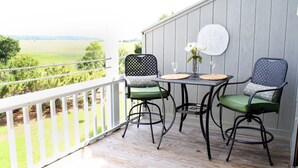 A balcony with two chairs and a table, overlooking a grassy field. - Peaceful Villa with Ocean and Hunting Island View (Harbor Island)