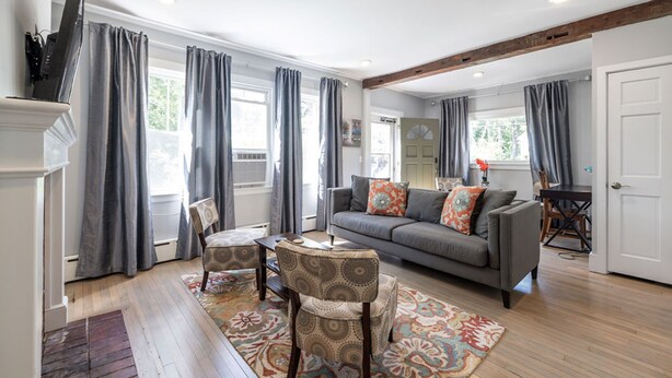 Un salon avec un canapé gris, des fauteuils à motifs, une table basse et une cheminée.