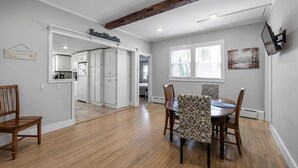 Un grand espace dédié à la salle à manger, avec une table en bois et des chaises à motifs, une cuisine en arrière-plan et un panneau indiquant « Coquillages ».