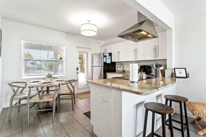 A modern kitchen with white cabinets, a central island, bar stools, and a dining area with chairs.