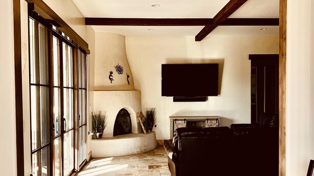 A spacious living area with a fireplace, a television mounted on the wall, and a large window with blinds.