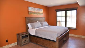 Une chambre avec un mur orange, un cadre de lit en bois, une table de chevet et une fenêtre donnant sur un beau paysage.