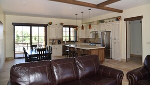 A spacious kitchen with white cabinets, a large island, and modern appliances. There is a dining area with a table and chairs, and a leather sofa in the foreground.