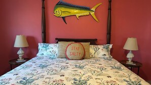 Een bed met een bloemenbedekking, twee nachtkastjes met lampen, een vis aan de muur en een kussen met de tekst 'STAY SALTY'.