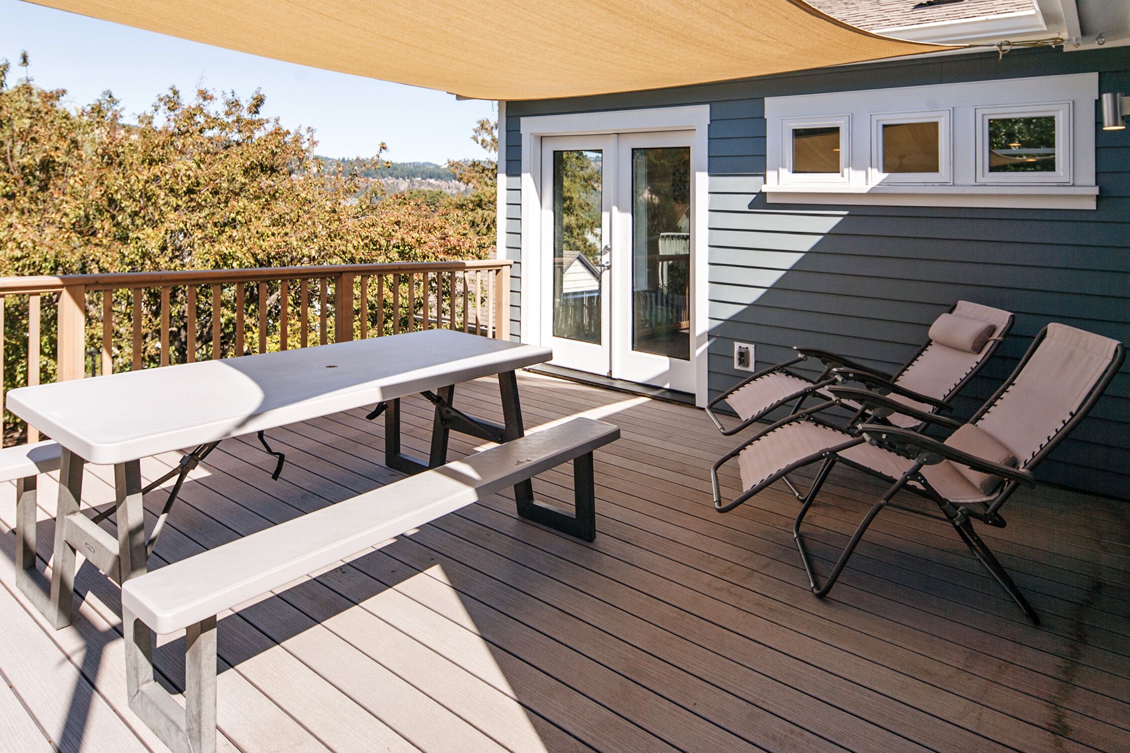 Une terrasse en bois avec une table de pique-nique et des chaises longues, une porte-fenêtre coulissante et une vue sur l’extérieur.