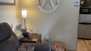 A living room with a sofa, a small table with decorative items, a lamp, and a wall-mounted macrame piece. - Julia's Cottage, peace @ Music Springs (Hawkins)
