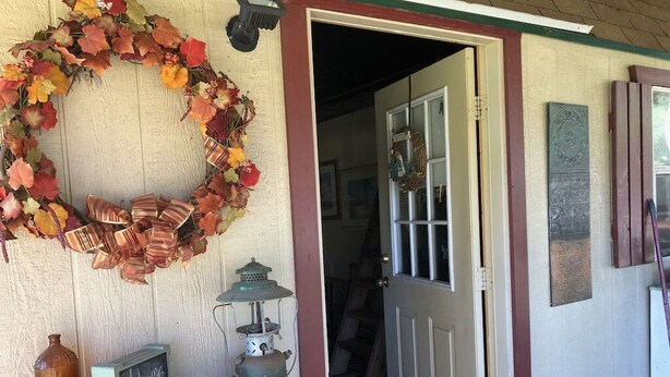 A wooden door with a decorative wreath, a vintage lantern, and a welcome sign on a shelf. - Julia's Cottage, peace @ Music Springs (Hawkins)