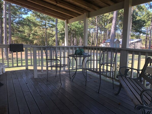 A covered porch with wooden flooring, metal chairs, a small round table, and a bench. - Julia's Cottage, peace @ Music Springs (Hawkins)