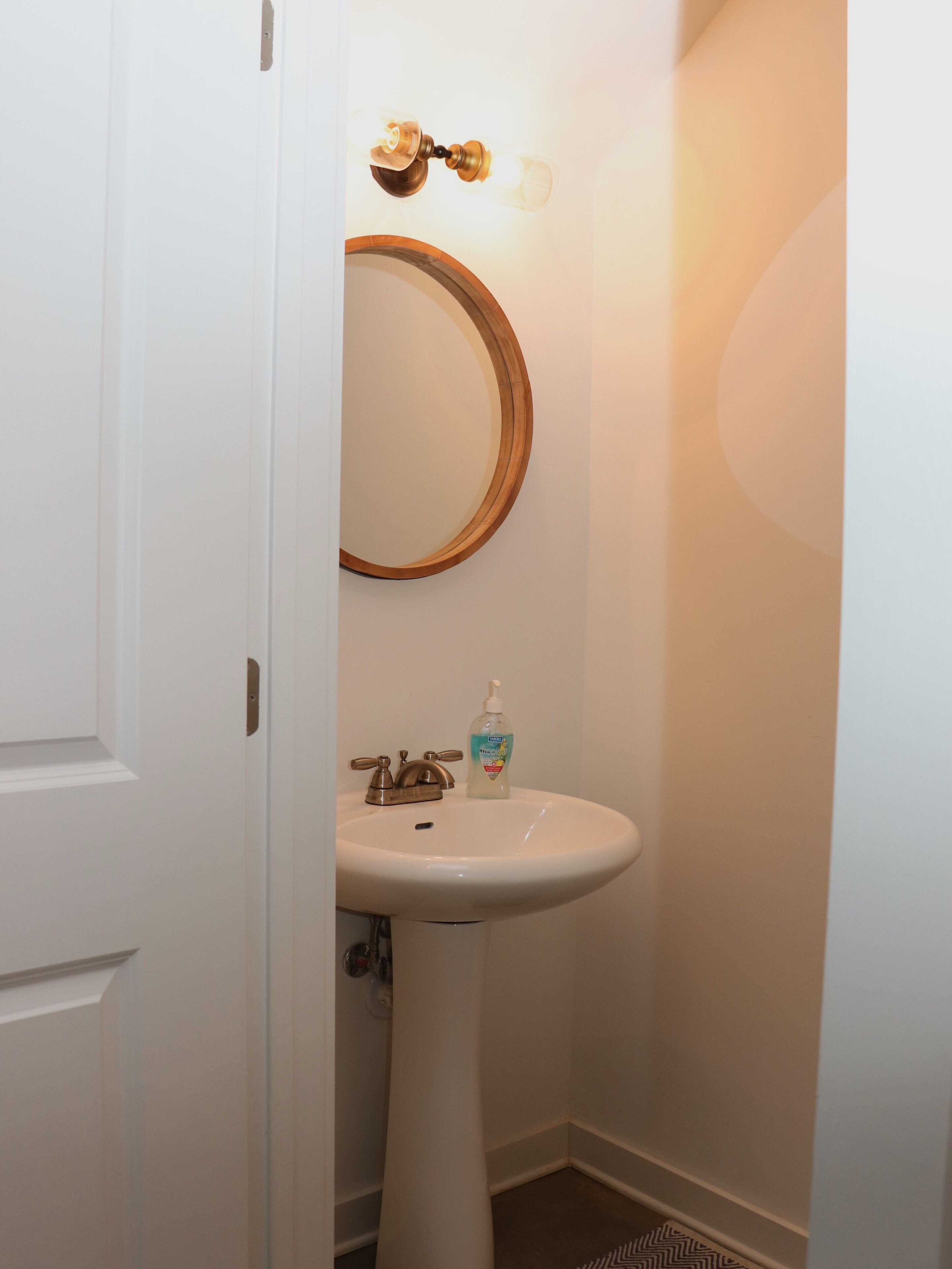 A bathroom with a white sink, a round mirror, and a bottle of hand soap.