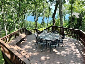 Eine Holzdar Terrasse mit einem Metalltisch und -stühlen, umgeben von Bäumen und mit Blick auf ein Gewässer.