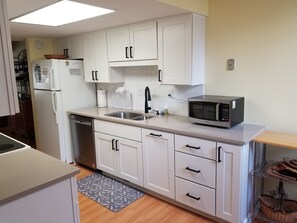 Cocina compacta con armarios blancos, un lavamanos de acero inoxidable, un microondas y un escurreplatos.