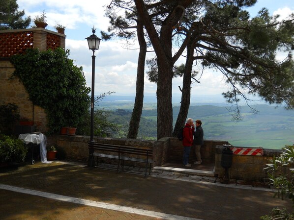 A stone bench with a metal lamp post, a stone wall with potted plants, and a view of a valley.