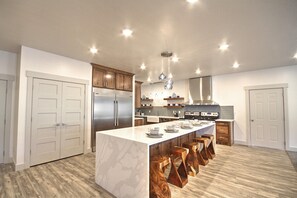 A modern kitchen with a large island, wooden bar stools, stainless steel appliances, and pendant lighting.