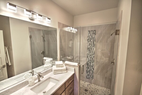 A modern bathroom with a glass-enclosed shower, a large mirror, and a marble countertop.