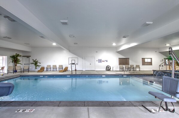 An indoor swimming pool with clear water, a basketball hoop, and several lounge chairs.