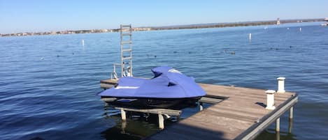 Ein Jet-Ski liegt an einer hölzernen Pier, die sich in ruhiges Wasser erstreckt, über dem ein klarer Himmel zu sehen ist.