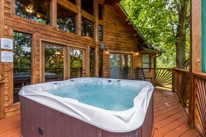 Relax in a hot tub surrounded by lush trees and a wooden structure.