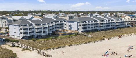 Un hôtel en bord de mer doté de nombreux balcons, d’une plage de sable et d’une promenade qui mène à la plage.