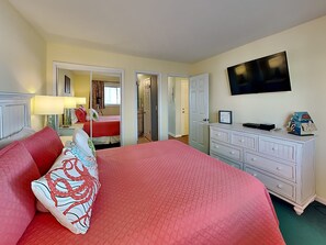 Ein Hotelzimmer mit einem großen Bett, einem Schminktisch, einem an der Wand befestigten Fernseher und einer Tür zu einem Badezimmer.