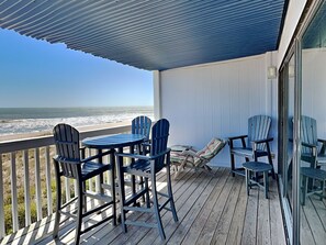 Eine Holzterrasse mit Adirondack-Stühlen und einem Tisch, mit Blick auf den Ozean.