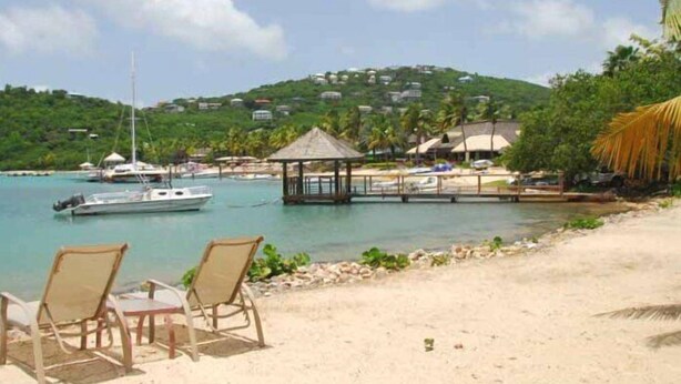 A beach with two lounge chairs, a small gazebo, and a dock with a sailboat. - String of Pearls Cozy Romantic Beach Front 1bedroom- Last Minute Discount! Ask! (Chocolate Hole)