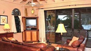 A living room with a brown leather sofa, a television, and a glass door leading outside. - String of Pearls Cozy Romantic Beach Front 1bedroom- Last Minute Discount! Ask! (Chocolate Hole)