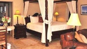 A four-poster canopy bed with white linens, a wooden headboard, and a nightstand with a lamp. - String of Pearls Cozy Romantic Beach Front 1bedroom- Last Minute Discount! Ask! (Chocolate Hole)