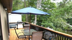 A wooden deck with a table and chairs, a grill, and an umbrella. - Affordable Private Lake Front House (Waleska)