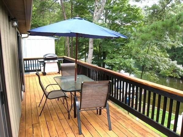 A wooden deck with a table and chairs, a grill, and an umbrella.