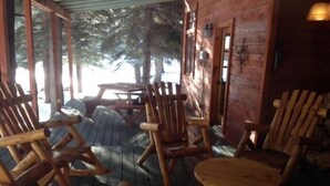 Eine Holzterrasse mit Adirondack-Stühlen und einem runden Tisch, mit Blick auf eine verschneite Landschaft.