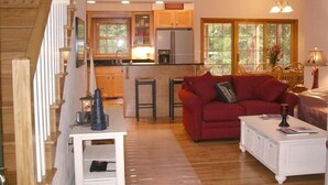A spacious living area with a red sofa, a white coffee table, and a kitchen in the background. - Walking distance to all you will need! Sleeps 8-10 (Ellison Bay)