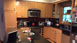 A kitchen with wooden cabinets, a black countertop, a microwave, a stove, and a refrigerator. - Walking distance to all you will need! Sleeps 8-10 (Ellison Bay)