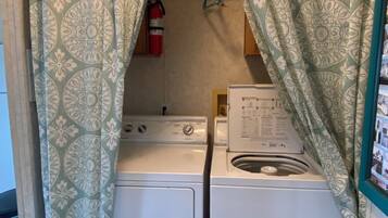 Un área de lavandería con dos lavadoras blancas, un extintor y cortinas estampadas.