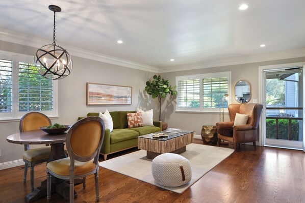 A living room with a green sofa, a wooden coffee table, and a dining table with chairs. - Close to Sonoma Plaza, Hot Tub and Bikes Included (Sonoma)
