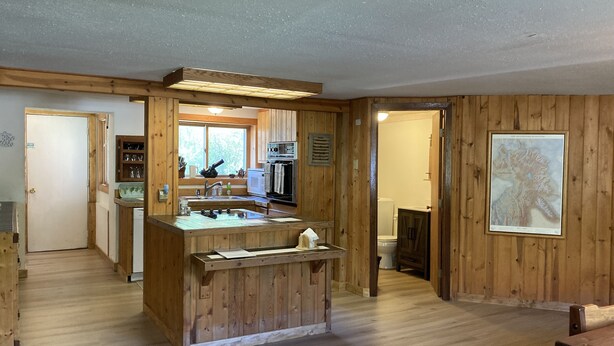 Interior de madera con cocina que incluye un lavamanos, estufa y armarios. Hay un mapa enmarcado en la pared y una puerta que da a otra habitación.