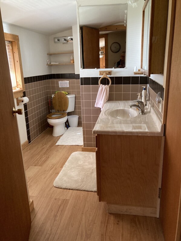 A compact bathroom with a wooden toilet, a sink, and a mirror. - Yellowstone Park - 1/2 Mile-Silver Gate (Silver Gate)