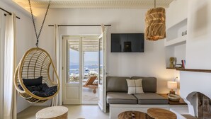 Un salon moderne avec un fauteuil suspendu en osier, un canapé, une table basse en bois et un téléviseur fixé au mur.